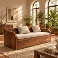 Daybed style sofa with swept wood sides, paneled base and a long seat pad in a bright living room with arched windows and plants