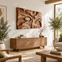 Deep carved wooden wall relief with an oval eye and flowing swirls in a bright sunroom with green plants