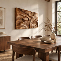 Deep carved wooden wall relief with an oval eye and flowing swirls beside a dining table in natural light