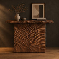 Wooden console table with a live edge top and a deeply carved front in a dark studio against a charcoal plaster wall