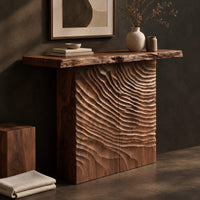 Corner detail of wooden console table with a live edge top and a deeply carved front beside wood, brass and linen samples