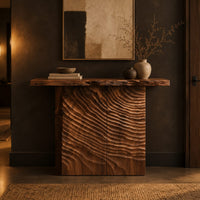 Wooden console table with a live edge top and a deeply carved front in a dark entryway at golden hour