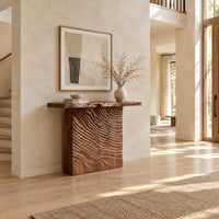 Wooden console table with a live edge top and a deeply carved front in a bright open plan entryway