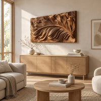 Wide carved wood relief panel of a sweeping feather with flowing layered barbs above a light oak sideboard in daylight