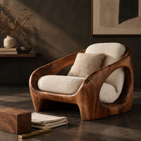 Corner detail of thick shell wooden chair with wide side openings and cream cushions beside wood, brass and linen samples