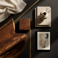 Corner detail of dark coffee table with a deep U shaped open shelf beside wood, brass and linen samples