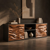Corner detail of low wooden sideboard with wave carved door panels and an open center bay beside wood, brass and linen samples