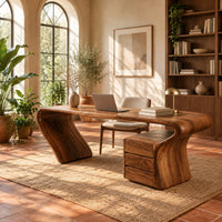 Desk with a top that flows into a slanted leg and drawer pedestal in a bright home office with arched windows and plants