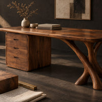 Corner detail of wide desk with a forked limb leg and a three drawer pedestal beside wood, brass and linen samples