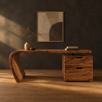 Desk with a single swept side leg and a two drawer cabinet in a dark studio against a charcoal plaster wall
