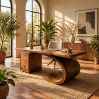 Desk with a sweeping scroll base and a three drawer pedestal in a bright home office with arched windows and plants
