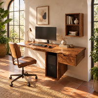 Wooden desk with a thick slab top and a hollow column support in a bright home office with arched windows and plants