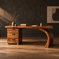 Wood desk with three stacked drawers and one sweeping curved leg in a dark studio against a charcoal plaster wall