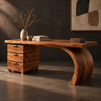 Corner detail of wood desk with three stacked drawers and one sweeping curved leg beside wood, brass and linen samples