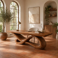 Wooden desk with a smooth slab top on a twisting infinity loop base in a bright home office with arched windows and plants