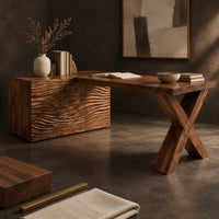 Corner detail of wooden desk with a wave carved cabinet block and an x shaped leg beside wood, brass and linen samples