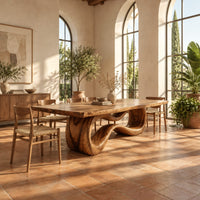 Rectangular dining table on a looping ribbon pedestal base in a bright dining room with arched windows and plants