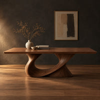 Dining table on a single sweeping pedestal with an oval opening in a dark studio against a charcoal plaster wall