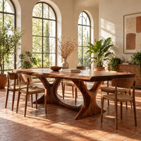Dining table with two branching legs and a wavy edged top in a bright dining room with arched windows and plants