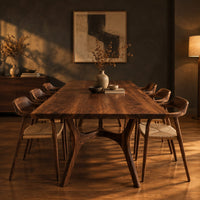 Rectangular dining table with splayed branching legs and an arched cross brace in a dark dining room at golden hour