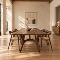 Rectangular dining table with splayed branching legs and an arched cross brace in a bright open plan dining room