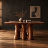 Dining table with a thick slab top on trunk shaped legs with arched openings in a dark studio against a charcoal plaster wall