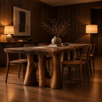 Dining table with a thick slab top on trunk shaped legs with arched openings in an evening dining room with walnut wall paneling