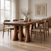 Dining table with a thick slab top on trunk shaped legs with arched openings in a Scandinavian dining room with white walls