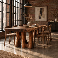 Dining table with a thick slab top on trunk shaped legs with arched openings in an industrial loft dining room with exposed brick