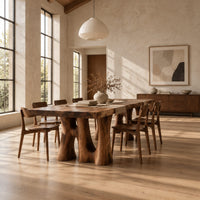 Dining table with a thick slab top on trunk shaped legs with arched openings in a bright open plan dining room