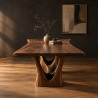 Dining table with a flared wavy top and a carved arch pedestal in a dark studio against a charcoal plaster wall