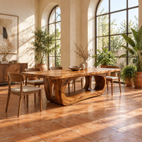 Rectangular dining table with a thick slab top on a hollowed oval base in a bright dining room with arched windows and plants