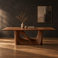 Dining table with a smooth rectangular top and a wave sculpted base in a dark studio against a charcoal plaster wall