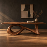 Long dining table on a sweeping ribbon base with one large oval opening in a dark studio against a charcoal plaster wall