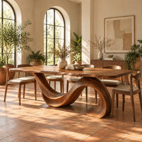 Dining table with a single sweeping wave base under a long slab top in a bright dining room with arched windows and plants
