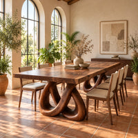 Dining table with two knotted loop pedestals and a thick slab top in a bright dining room with arched windows and plants