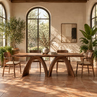 Dining table with twin sculpted arch legs and a smooth slab top in a bright dining room with arched windows and plants