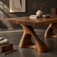 Corner detail of dining table with a thick plank top on two sculpted loop pedestals beside wood, brass and linen samples
