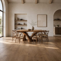Dining table with a thick plank top on two sculpted loop pedestals in a bright open plan dining room