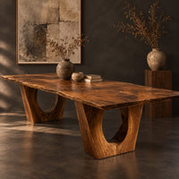 Corner detail of long dining table on two heavy pedestals with arched openings beside wood, brass and linen samples