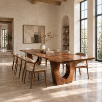 Long dining table on two heavy pedestals with arched openings in a bright open plan dining room