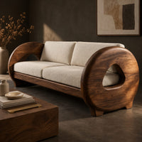 Corner detail of sofa with thick circular wooden arms, hollow cutouts and cream seat cushions beside wood, brass and linen samples