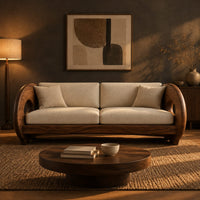 Sofa with thick circular wooden arms, hollow cutouts and cream seat cushions in a dark living room at golden hour