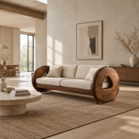 Sofa with thick circular wooden arms, hollow cutouts and cream seat cushions in a bright open plan living room