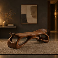 Bench with a dished seat and sculpted legs with oval cutouts in a dark entryway at golden hour
