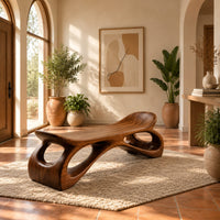 Bench with a dished seat and sculpted legs with oval cutouts in a bright entryway with arched windows and plants