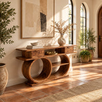 Console table with a double loop base and two small drawers in a bright entryway with arched windows and plants