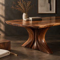 Corner detail of dining table with a long top and two flared sculpted pedestals beside wood, brass and linen samples