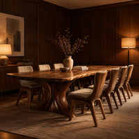 Dining table with a long top and two flared sculpted pedestals in an evening dining room with walnut wall paneling