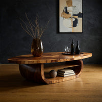 Oval coffee table on a drum base with an open shelf in a dark studio against a charcoal wall